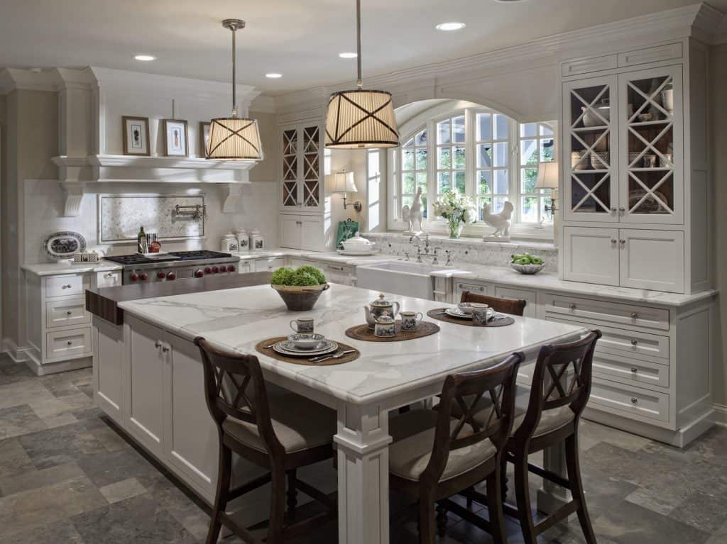 Custom rustic white kitchen boasting white marble countertops with an island and chairs