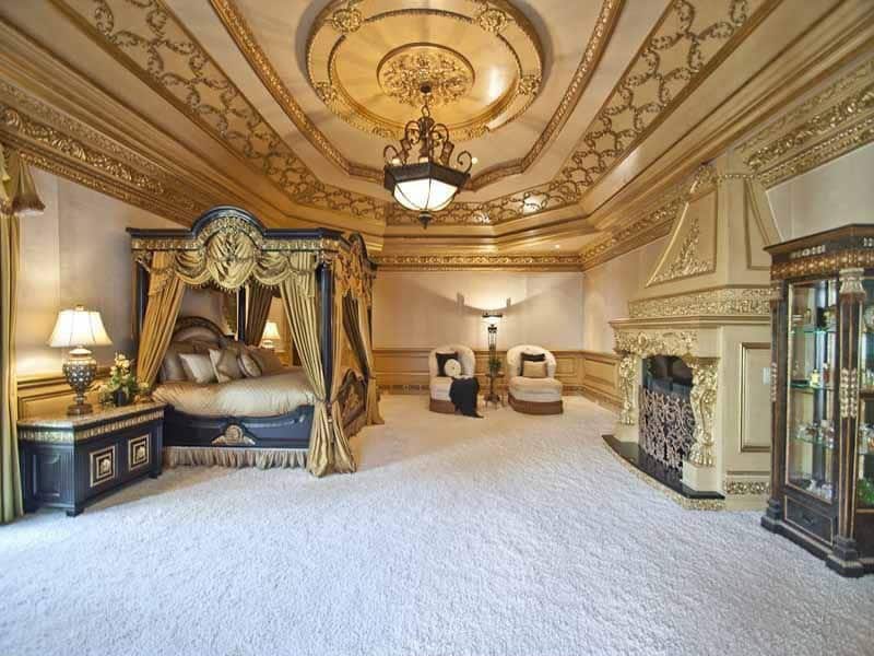 This traditional master bedroom has a gorgeous golden canopy that matches its golden fireplace. Enriched with intricate crown molding this room was designed for a king.